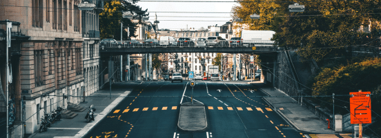 Route urbaine suisse avec passage piéton et bâtiments historiques sous un pont ferroviaire