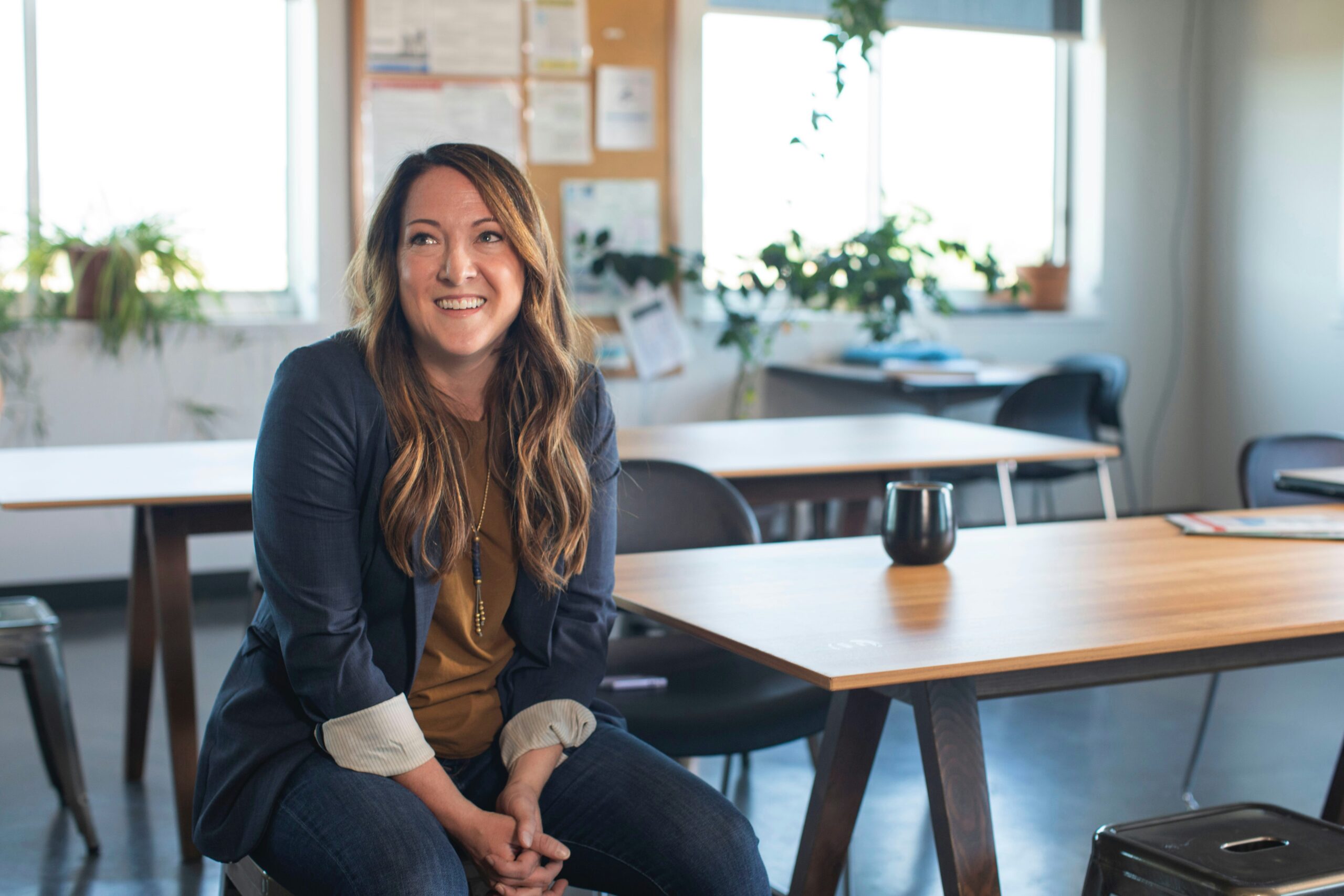Femme souriante en blazer bleu assis à un bureau dans un bureau moderne et lumineux